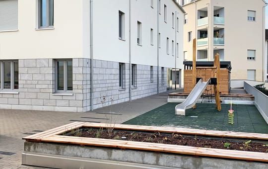Der Außenbereich umfasst Gemeinschaftsflächen mit Sitzbänken und einen Spielplatz.